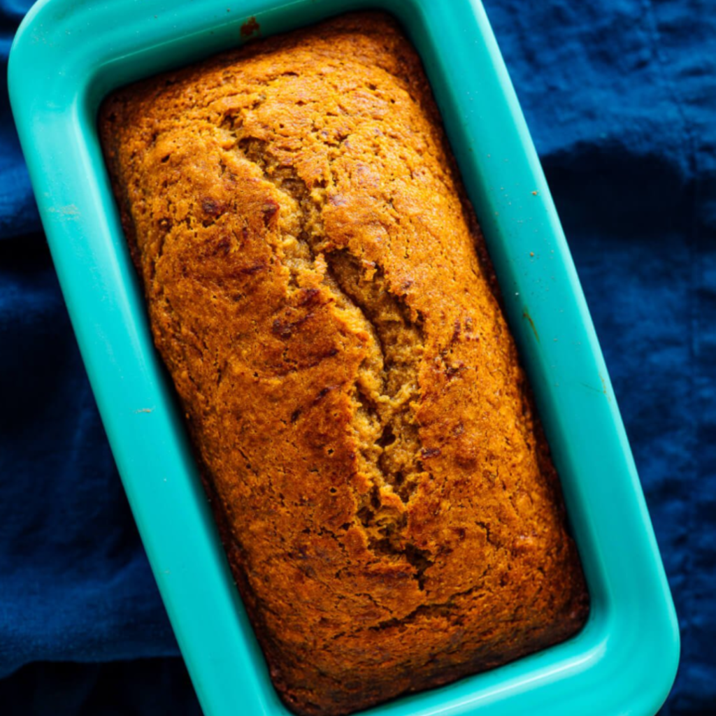 A freshly baked loaf of banana bread in a turquoise baking pan on a deep blue background.