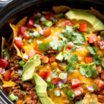 Cheesy crockpot taco casserole with tortilla chips, avocado, and green onions.