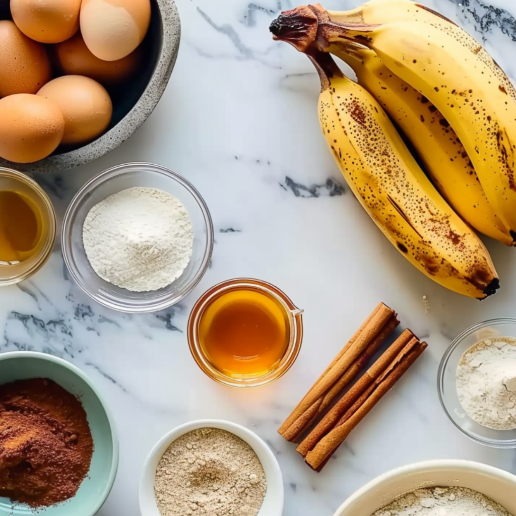 A collection of banana bread ingredients, including ripe bananas, eggs, flour, honey, cinnamon sticks, and other baking essentials, arranged on a marble countertop.